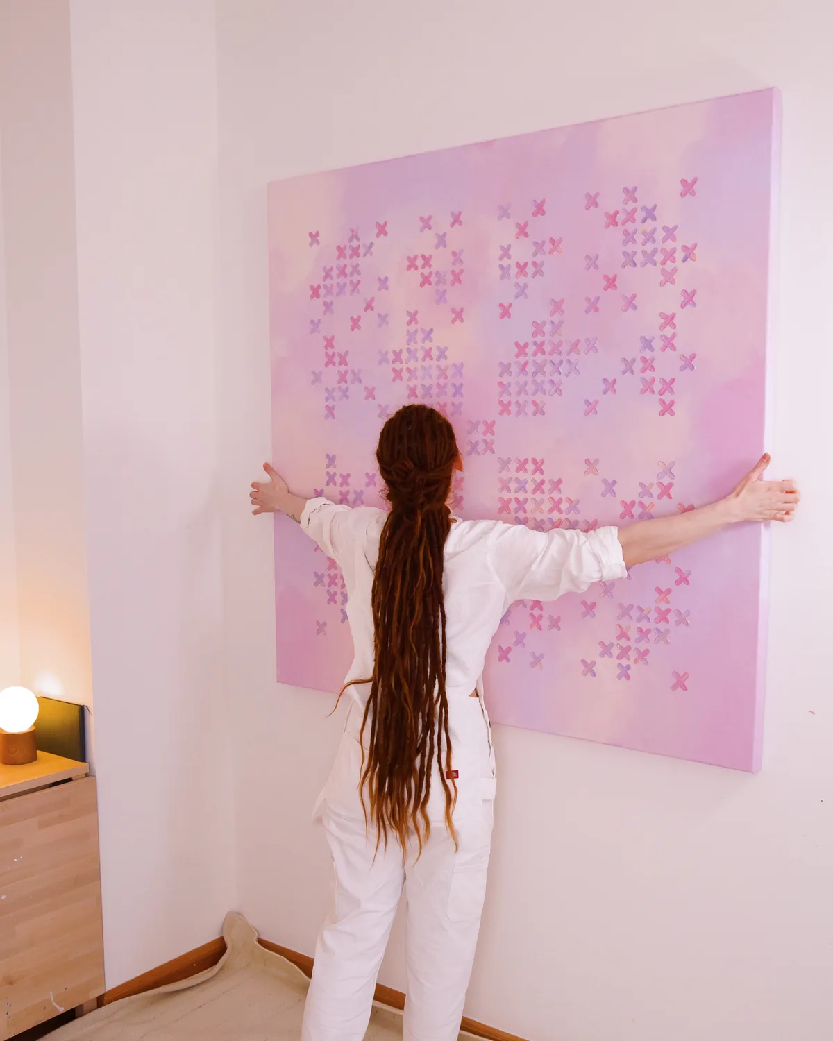 Alicja Suska standing in front of her painting Purple Sunset, arms outstretched